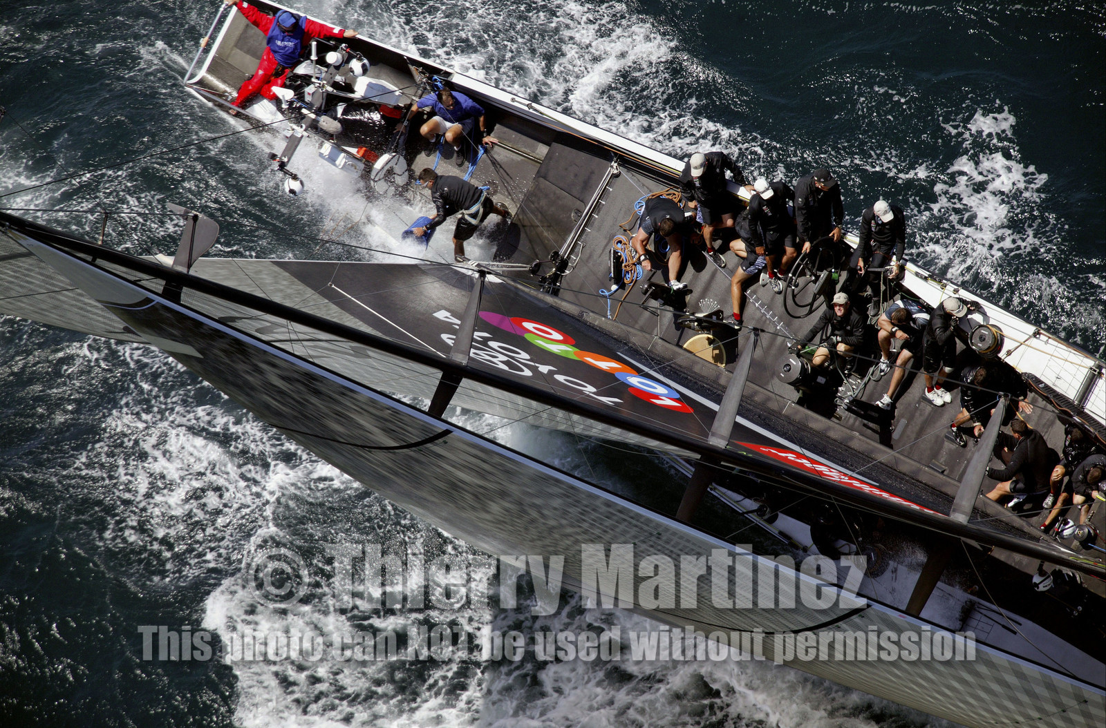 03_0169D ©Th.Martinez - Auckland (NZ) . America's Cup 2003. 15th February 2003. Day 1..Alinghi (SUI 64) vs Team NZ (NZL 82) .NZL 82 in first minutes of Race 1 before retiring on damage.  .Matt Mitchell (Team NZ midbowman) bailing water out of NZL 82. .